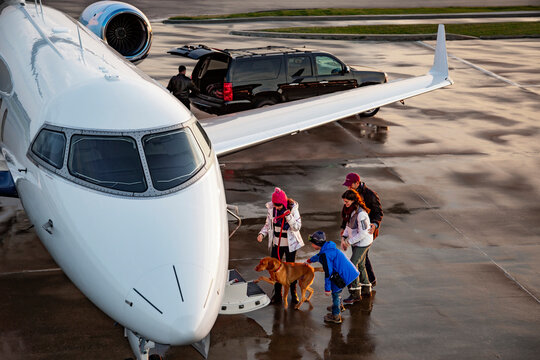 High angle view of Family with dog boarding private plane on wet tarmac of private airport for family vacation , pilot in background unloading luggage from SUV 
