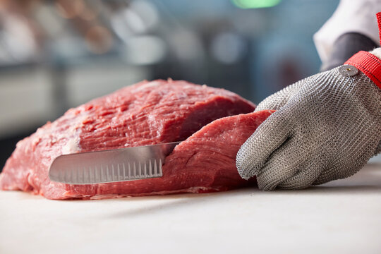 Detail of butcher slicing through side of beef, behind counter of meat market of grocery store 