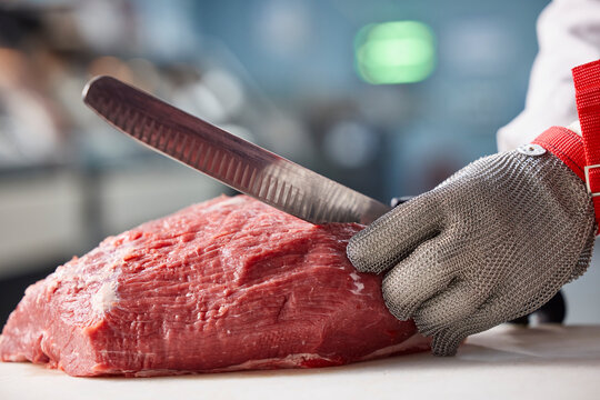 Detail of butcher making cuts of beef, behind counter of meat market of grocery store