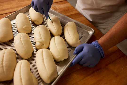 Detail of baker in kitchen of grocery store preparing tray of Bolillos (a type of savory bread made in Mexico and Central America) to go into the oven.
