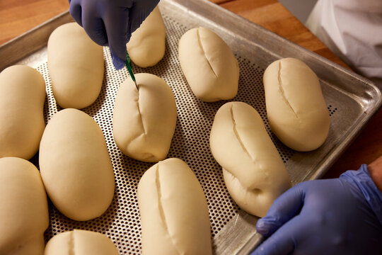 Close up detail of baker in kitchen of grocery store preparing tray of Bolillos (a type of savory bread made in Mexico and Central America) to go into the oven.