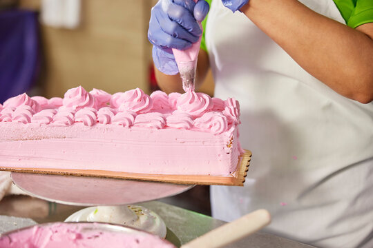 Close up detail of female baker adding frosting using a piping bag to layer cake in latin market bakery