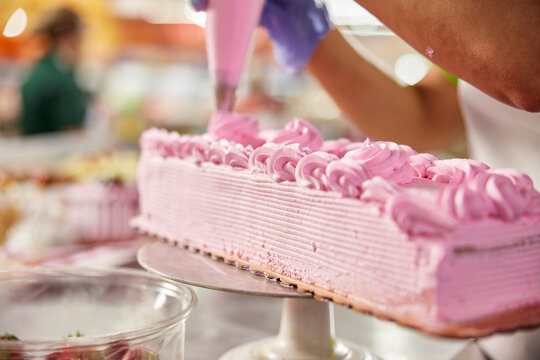 Low Angle close up detail of female baker adding frosting using a piping bag to layer cake in latin market bakery