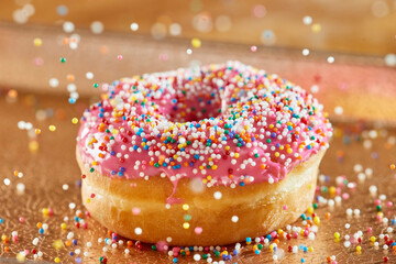 Close up detail view of donut with pink icing with decorative rainbow sprinkles falling into place