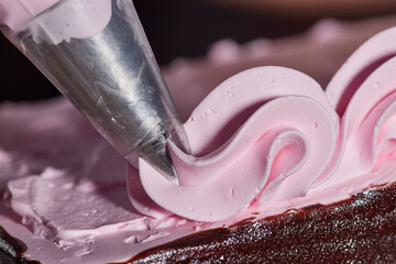 Close up detail of piping bag adding strawberry frosting accents to chocolate layer cake