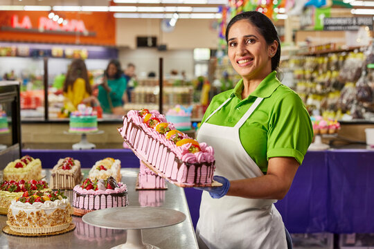 Female baker showing off finished layer cake after putting on the finishing touches of fresh fruit in latin market bakery.