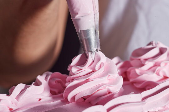 Close up detail of piping bag adding strawberry buttercream flower accents to chocolate layer cake