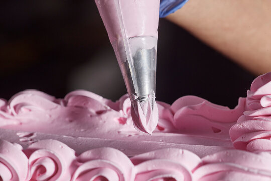 Close up detail of piping bag with icing tip adding strawberry buttercream flower accents to chocolate layer cake