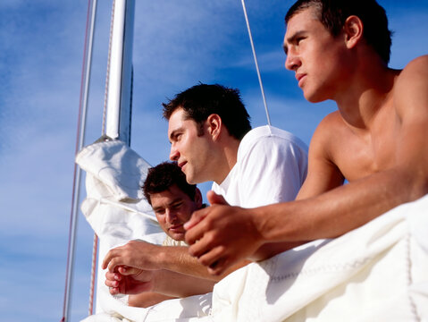 Three young male crew members leaning on the sail and boom catching up 