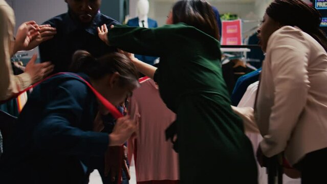 Security officer calms crowd on black friday sales rush, pushing people back and trying to control clothing store entrance. Clients shoppers being impatient, obsessed with cheap prices.