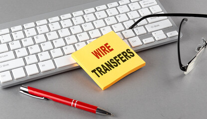 WIRE TRANSFERS text on a sticky with keyboard, pen glasses on grey background