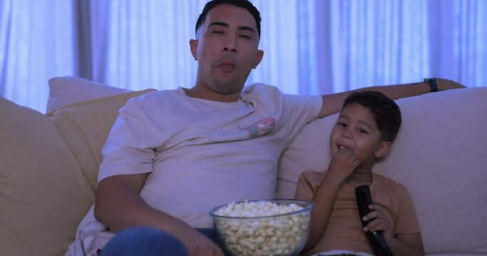 Movie, father and boy on a couch, popcorn and relax with happiness, quality time or bonding. Family, dad and male parent with kid on a sofa, child or watching tv with snacks, night or streaming films