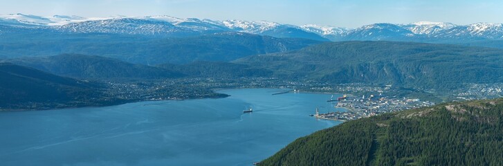 Panorama of ship leaving Mo i Rana through Ranfjorden, Helgeland, Norway. High megapixel image of big boat in fjord between high norwegian mountains in summer. View from Hauknestinden, snow on fjell.