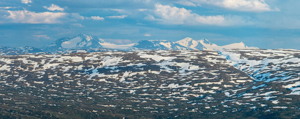 View from the peak of Hauknestinden, Mo i Rana, Helgeland, Norway, looking south towards Okstindan, the tallest mountain in Nord-Norge. Snow capped mountains in summer scandinavia. Panorama, hiking