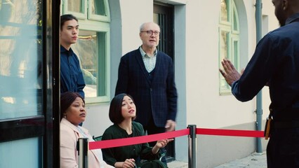 Crowd of people outdoors in line, gathering in the morning and wait to open clothing store door. Anxious customers at entrance on black friday, security guard trying to calm clients.