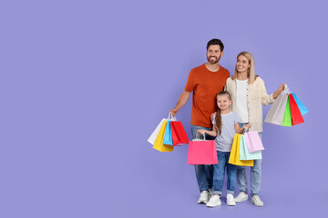 Family shopping. Happy parents and daughter with many colorful bags on violet background. Space for text