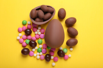 Delicious chocolate eggs and candies on yellow background, flat lay