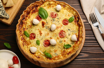 Delicious quiche with mozzarella cheese, tomatoes and basil on wooden table, flat lay