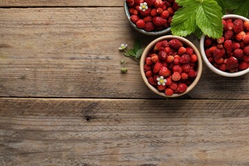 Fresh wild strawberries in bowls and leaves on wooden table, flat lay. Space for text