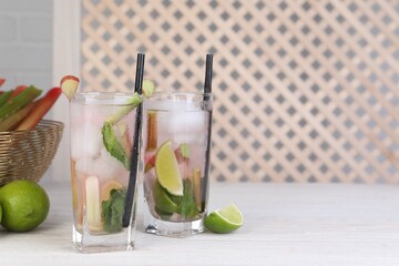 Tasty rhubarb cocktail with lime on white wooden table, space for text