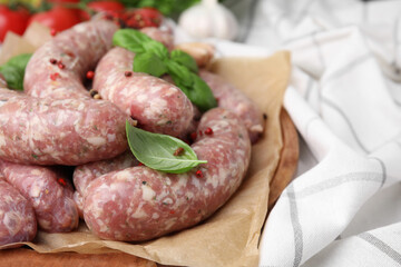Raw homemade sausages, basil leaves and peppercorns on table, closeup