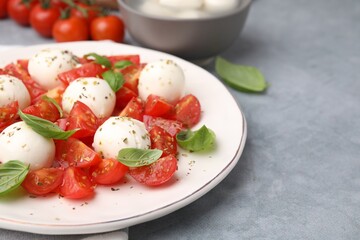 Tasty salad Caprese with tomatoes, mozzarella balls and basil on grey table, closeup. Space for text