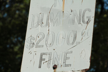 old worn and faded dumping $2000 fine sign with light black writing on rectangle white background...