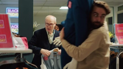 Store worker trying to calm crazy people rushing to get best deals on clothing items, excited crowd on customers in a hurry for black friday promotions. Shoppers grabbing clothes. Handheld shot.