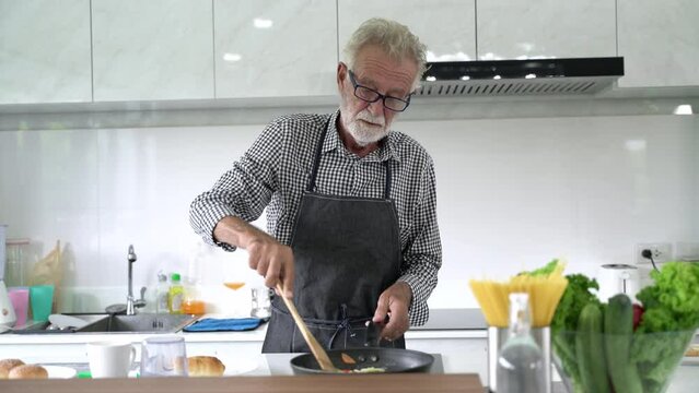 Senior man while cooking in kitchen at home. Mature enjoying cooking food.