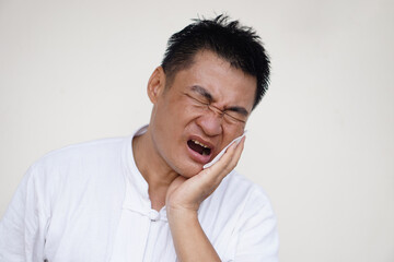 Fototapeta premium Asian man suffers from painful toothache, gum inflammation, use hand to touch his cheek, close eyes, open mouth. Concept, dental health problem and health care. 