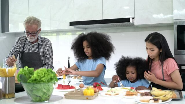 Senior man and african children with family while cooking in kitchen. Mature and girl enjoying cooking food togetherness.