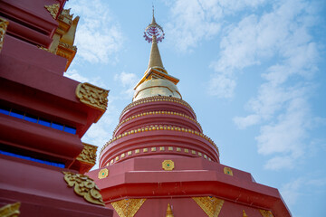 Red Thai Chedi or pagoda in northern temple in Thailand with blue sky and some construction in foreground of picture.