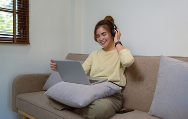 young woman in headphones using laptop listening to music relax relax sitting on the sofa at home