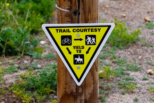Triangular yellow trail courtesy sign on a wood post giving yield instructions
