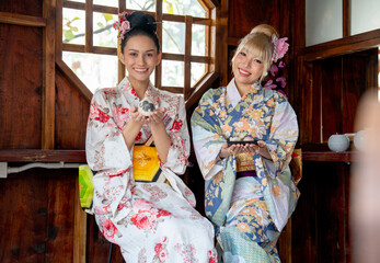 Portrait of two Asian women wear japanese style dress sit and enjoy in small shop and also hold small gift and look to camera with smiling.