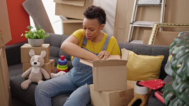 Young pregnant woman packing toys and clothes of cardboard box at new home