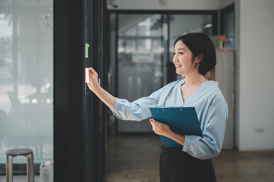Smiling businesswoman sticking adhesive notes on glass window in office.