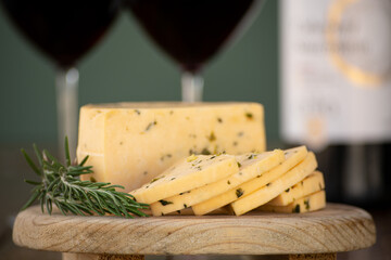 Queso manchego con epazote sobre una tabla de madera y copas de vino al fondo lacteos