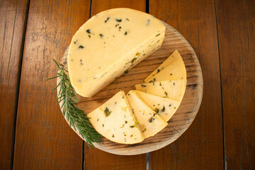 Toma zenital de un queso manchego entero y en rodajas sobre una tabla de madera con epazote 