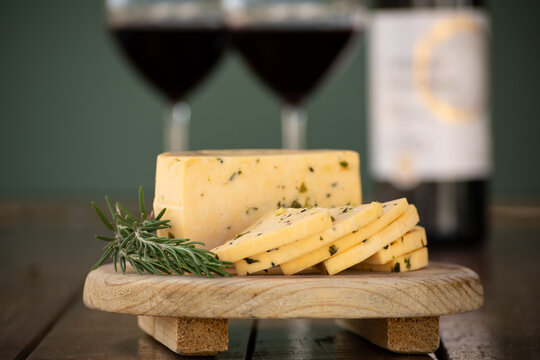 Queso manchego con epazote sobre una tabla de madera y copas de vino al fondo delicioso aperitivo
