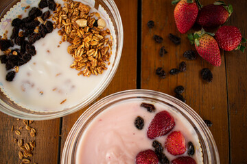 Yogurt natural y de fresa con cereales fresas y pasas sobre una mesa de madera en una toma zenital 