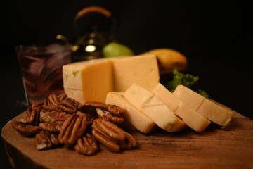 Bandeja de quesos fresco manchego con nuez en un bodegon sobre una tabla de madera y frutas fondo color negro aislado
