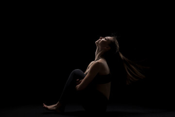 cute caucasian girl sitting with her hair in the air against dark backgroung. side lit silhouette..