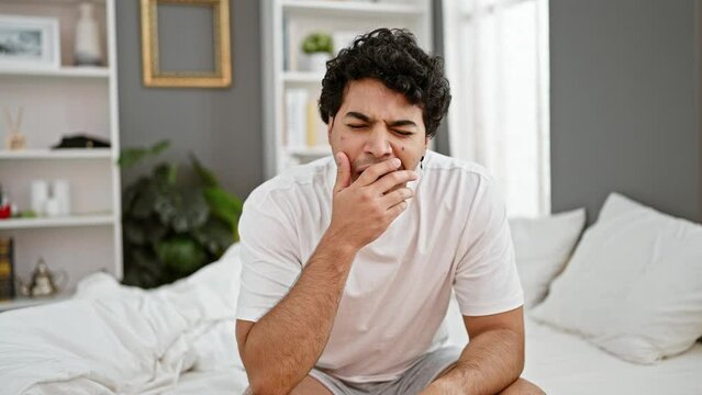 Young latin man tired stretching arms yawning at bedroom