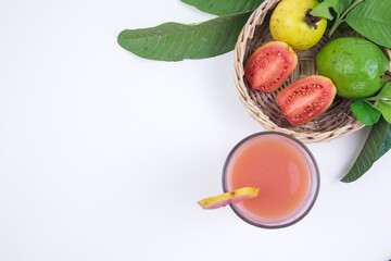 Guava juice and fresh red guava in a woven bamboo basket with green leaves on a white background