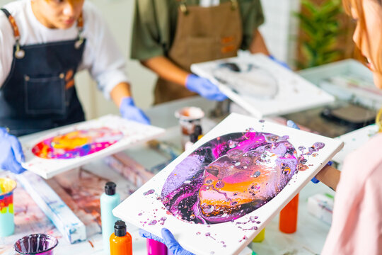 Group of Asian generation z people learning acrylic pouring art on canvas workshop at art studio. Young artist university student enjoy and fun creating colorful abstract modern art painting in class.