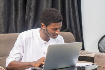 Young man smiling as he reads the screen of a laptop computer while relaxing on a comfortable couch at home