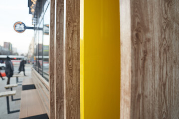 A fragment of a wall at the intersection of several natural-colored boards, a view of the street along the wall. Unrecognizable people near the cafe. High quality photo