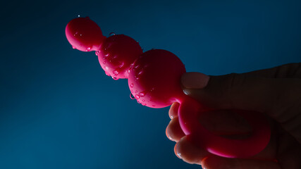 Woman holding pink anal beads in drops of water on a blue background. Sex toy hygiene concept.