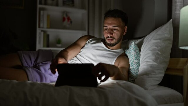 Young arab man using touchpad lying on bed at bedroom